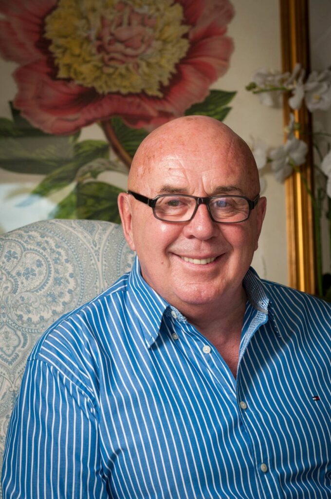 Sergio wears a blue button-up shirt and glasses and smiles directly at the camera